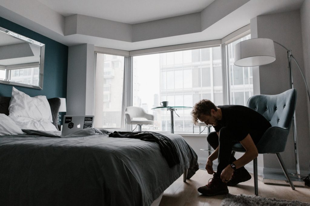 Image of a man getting dressed in his bedroom late in the day. On the bed is an open laptop. He is building his digital life.
